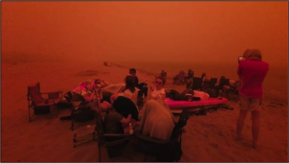 People on a beach huddling from smoke and fire.